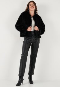 Black faux fur jacket with a rounded neckline, wide sleeves, and a soft texture, paired with sleek black faux leather trousers and high-heeled boots.