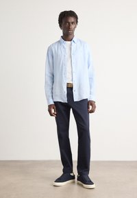 Lichtblauw overhemd, witte T-shirt eronder, marineblauwe broek en marineblauwe schoenen met een lichte zool. Casual outfit op een staande mannelijke model.