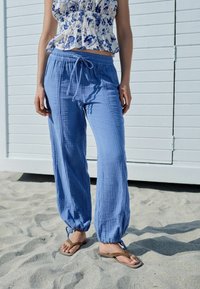 Lichtblauwe, losse broek gemaakt van gestructureerde stof met een elastische tailleband en trekkoord; heeft taps toelopende pijpen metGathered cuffs.
