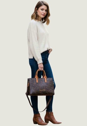 Brown patterned handbag with gold hardware, tan handles, cream sweater, blue jeans, and brown ankle boots. Casual outfit displayed.