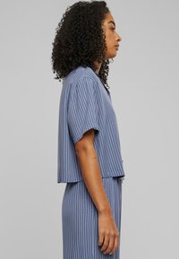 Cropped blue striped shirt with short sleeves and wide cuffs, made of lightweight fabric. Features a button-down front and relaxed fit.