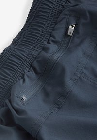Pantaloncini sportivi blu navy con cinturino elasticizzato arricciato, dotati di tasca con zip e tessuto liscio e resistente con una texture sottile e dettagli di cucitura.