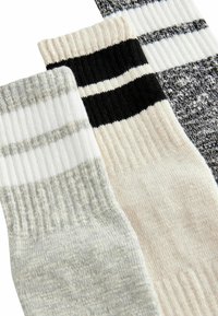 Tre par strumpor: grå med vita ränder, ljusbeige med svarta ränder och en strukturerad svart med vita ränder. Alla har ribbade mudd.