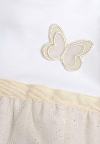 Weißes Kleid mit einem durchsichtigen Schmetterlings-Applikation und einem beigen Band in der Taille. Der Rock hat eine Tüll-Überlagerung mit goldenen Sprenkeln.