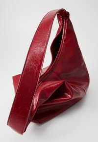 Weiche rote Leder-Schultertasche mit breitem Tragegurt und lässiger, ungegliederter Form auf weißem Hintergrund.