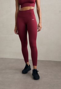 Burgunderfargede ribbede leggings med høy midje og logodetalj, paret med svarte treningssko. Glatt, elastisk stoff.