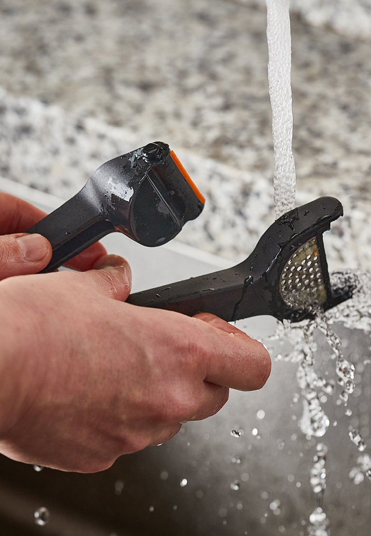 Schwarze Küchenutensilien werden unter fließendem Wasser abgespült. Eines ist ein Schäler mit einem orangefarbenen Akzent und das andere eine Reibe mit einer strukturierten Oberfläche.