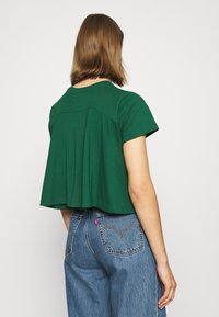 T-shirt vert à manches courtes avec une coupe ample, un col arrondi et des détails de couture à l'arrière, associé à un jean bleu taille haute.