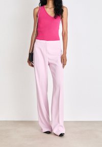 Różowy prążkowany top na ramiączkach z dekoltem w serek, zestawiony z jasnoróżowymi szerokimi spodniami. Czarne płaskie buty i mała czarna torebka na łańcuszku.