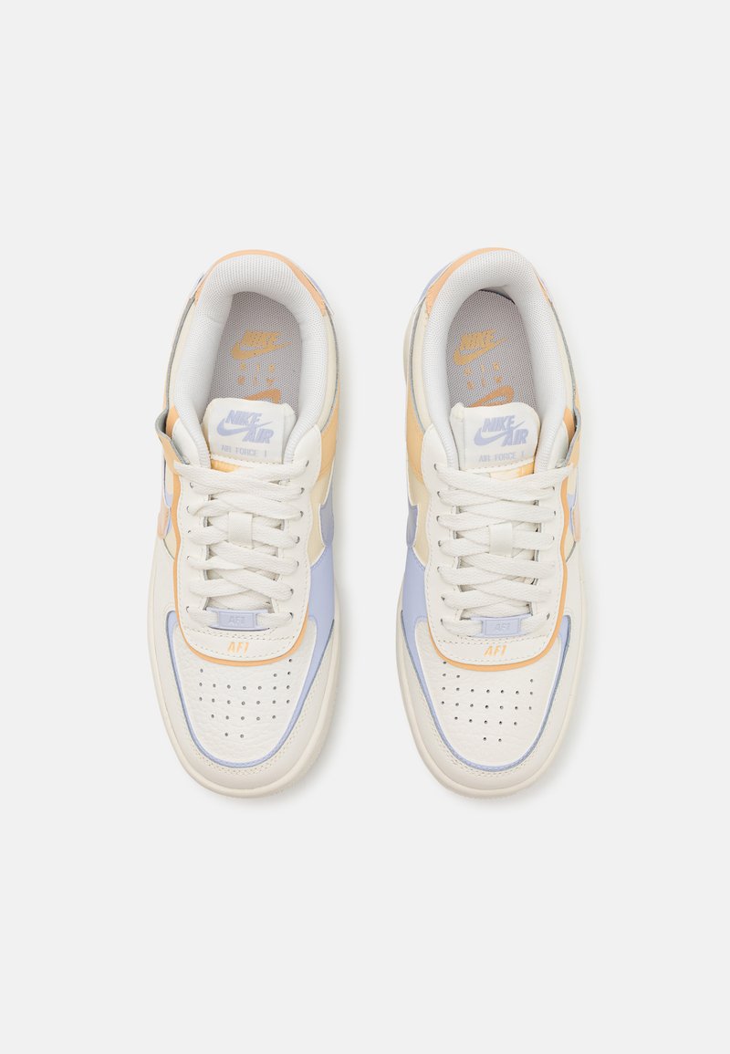 Zapatillas Nike Air Force 1 en blanco, naranja claro y azul pastel. Presentan cuero texturizado, puntera perforada y cordones planos.