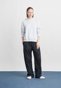 Felpa azzurra con cappuccio e tasca frontale, abbinata a pantaloni neri con cuciture rosse a contrasto. Tessuto morbido e vestibilità comoda.