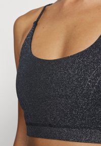 Sutien desportivo em tecido escuro e cintilante. Apresenta um decote em forma de scoop, alças finas e um design ajustado com uma textura suave e bordas sem costura.