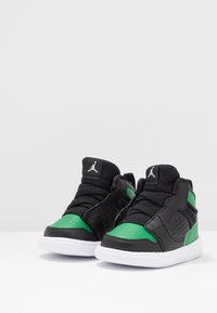 Pár černých a zelených vysokých tenisek Jordan s bílými podrážkami, malá velikost vhodná pro batolata nebo malé děti.