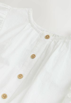 Fehér pamut blúz kerek nyakkivágással, gombos fodorral, fából készült gombokkal és texturált virágmintákkal.