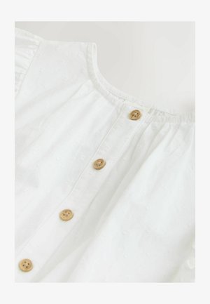 Fehér pamut blúz kerek nyakkivágással, gombos fodorral, fából készült gombokkal és texturált virágmintákkal.