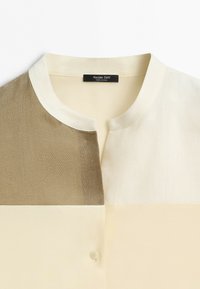Košile s límečkem s barevným blokovým designem v béžové, smetanové a světle hnědé barvě, s jedním knoflíkem pod výstřihem.