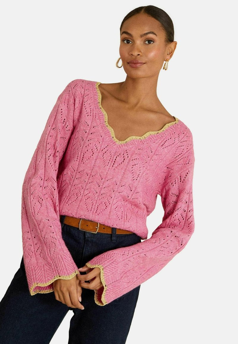 Roze gebreide trui met een V-hals, een ingewikkeld kantpatroon en een gekartelde gele boord bij de kraag en mouwen. Lange klokvormige mouwen.