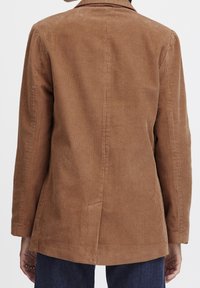 Brun kordflöjtsblazer med en strukturerad yta, enkel rygghalsöppning och skräddarsydd passform. Har långa ärmar och slagkragar.