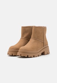 Bottines en suede tan avec un bout arrondi, une semelle en caoutchouc épaisse et un design minimaliste. Présente un détail de couture autour de la tige.