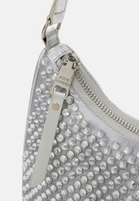 Sølv håndtaske med en struktureret overflade prydet med runde rhinsten. Har en lynlåslukning, metalhardware og en glat rem.