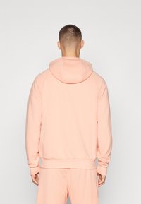 Lys rosa hettegenser med en tilpasset hette og ribbestrikkede mansjetter og hem. Har et avslappet design med en jevn tekstur og løs passform.