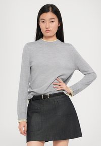 Grauer Strickpullover mit runder Halsausschnitt und langen Ärmeln, kombiniert mit einem schwarzen Rock mit zwei vorderen Taschen und einem schwarzen Gürtel.