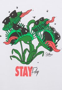 Vihreät sarjakuvamaiset venusloukkujat mustilla aurinkolaseilla ja punaisilla kielillä, valkoisella taustalla. Teksti lukee "STAY Fly" punaisella ja mustalla.