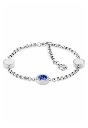 Silbernes Gliederarmband mit rundem blauen Stein als Mittelpunkt und zwei kreisförmigen silbernen Scheiben, auf denen Text eingraviert ist, vor weißem Hintergrund.