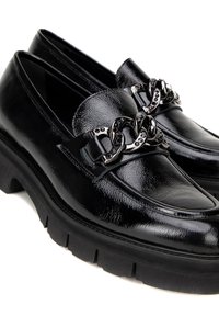Zwarte gepatineerde leren loafers met een chunky rubberen zool, voorzien van een decoratieve metalen kettingaccent aan de voorkant. Gladde textuur, klassiek ontwerp.