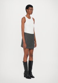 Hvit ermeløs topp, grå tweed skjørt med en lett A-linjeform, og svarte knee-high hæl støvler med et elegant design.