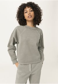 Sudadera gris clara hecha de una tela suave, con cuello redondo, mangas raglán y puños acanalados. Combinada con pantalones de chándal a juego.