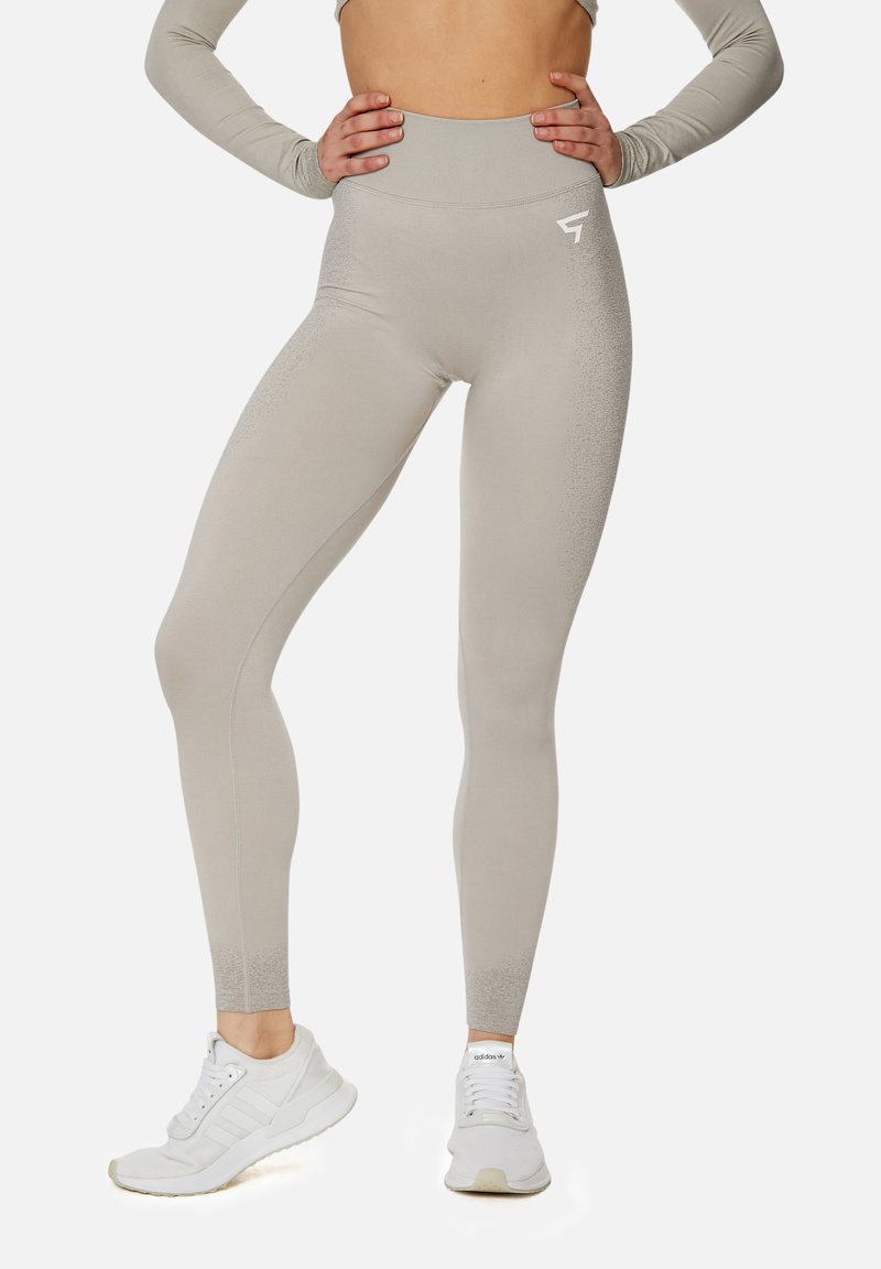 Hoch taillierte, hellgraue Leggings aus einem glatten Stoff mit dezenten Texturdetails an den Knöcheln; kombiniert mit weißen Sportschuhen.