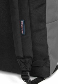 Sac à dos noir et gris en tissu durable, avec des bretelles ajustables, une étiquette de logo et un clip pour sécuriser les objets.