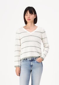 Hvit strikket genser med grønne striper, V-halsdesign, lange ermer og ribbestrikkede ermer. Kombinert med blå denimjeans.