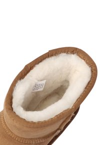 Brauner Wildleder-Ankle-Boot mit einem weichen, weißen Fellfutter, das am Einstieg sichtbar ist. Gibt ein Logetikett innen mit Größeninformationen.