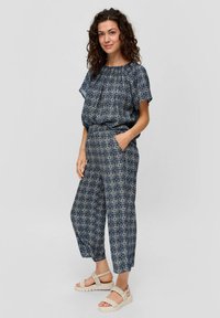 Navy-gekleurd jumpsuit met korte mouwen, elastische tailleband en zijzakken, gecombineerd met lichtgekleurde sandalen. Soepele stoftextuur.