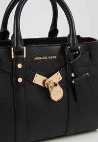 Černá texturovaná kožená kabelka se zlatými detaily, obsahující zámek a klíč, logo na přední straně a dvojité krátké uchy.