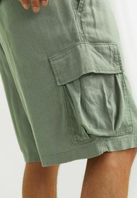 Shorts cargo vert clair en tissu doux et texturé. Dispose de grandes poches latérales et d'une coupe décontractée. L'ourlet est fini par une couture soignée.