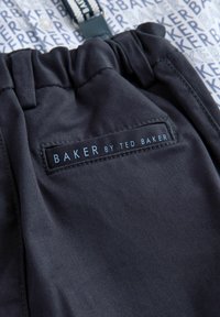 Granatowe spodnie z elastycznym paskiem w talii, z czarną etykietą z napisem "BAKER by TED BAKER." Gładka tekstura z delikatnym połyskiem.