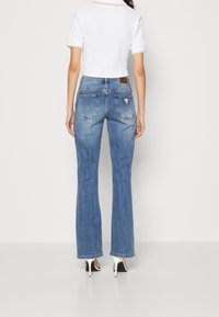 Jean flare en denim bleu moyen avec une finition délavée, taille haute, cinq poches et un petit logo sur la poche arrière.