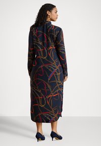 Sieviete ar tumšiem cirtainiem matiem, valkājot garu tumši zilu kleitu ar sarkaniem un brūniem ķēžu un virvju rakstiem, pieskaņotas tumši zilas zābaku papēžus, raugoties sāniski.