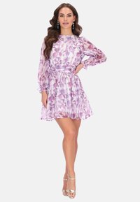 Bloemenjurk in paarse en roze tinten, met lange mouwen, gerimpelde lagen en een tailleriem. Gecombineerd met zilveren hakken.