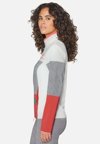 Fleece zip-up jack in lichtgrijs, rood en wit. Heeft gemusterde grijze mouwen, een hoge kraag en een ritszak aan de voorkant.