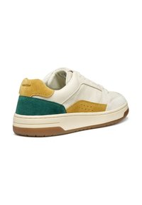 Zapatilla de cuero blanca con acentos de ante verde y mostaza. Presenta una suela acolchada, lados perforados y un diseño de punta redondeada.