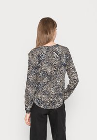 Blusa a maniche lunghe con fondo nero caratterizzata da un motivo casual di pois crema e blu, realizzata in tessuto leggero, con orlo arrotondato.