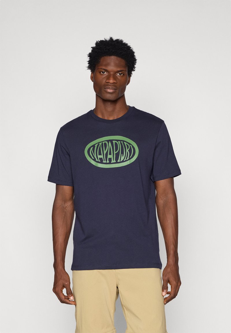 T-shirt en coton bleu marine avec un grand logo ovale vert et le texte "NAPAPIJRI" au centre. Manches courtes et col rond.