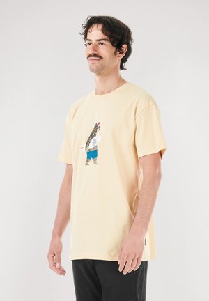 Kurzärmeliges, hellgelbes Baumwoll-T-Shirt mit einem Bärenmotiv in Surfbekleidung, blauen Shorts und Kappe sowie dezenten Texturdetails.