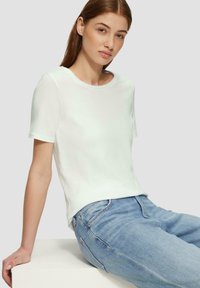 T-shirt blanc à manches courtes avec un col ras du cou, texture douce et coupe décontractée, associé à un jean en denim bleu clair.
