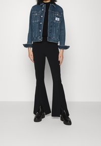 Džínová bunda v tmavě modré barvě se dvěma předními kapsami a logem, spárovaná s černými rozšířenými kalhotami s postranním rozparkem a masivními černými botami.