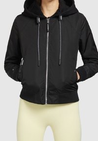 Czarna bomberka z kapturem, zapinana na zamek, z elastycznymi mankietami i sznurkami do ściągania. Posiada gładką teksturę oraz boczne kieszenie dla wygody.